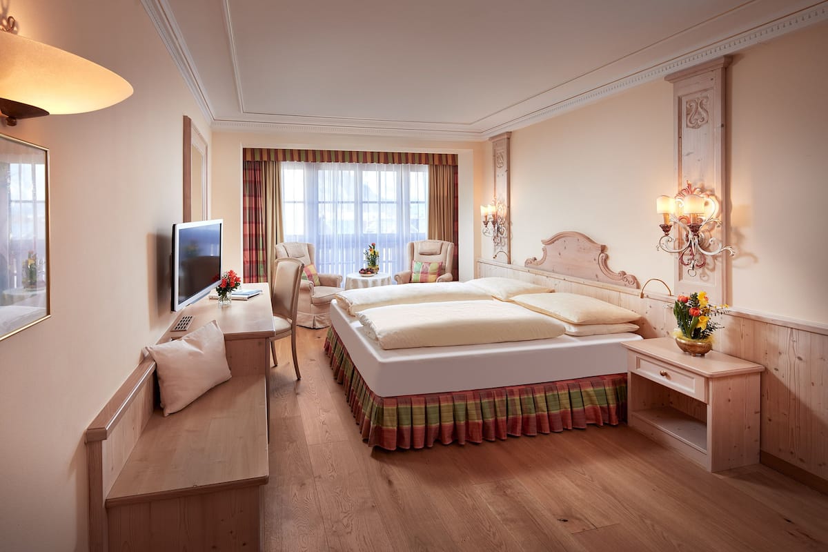 Een hotelkamer met een groot bed, een bureau met een computer, een stoel en een nachtkastje met een lamp.