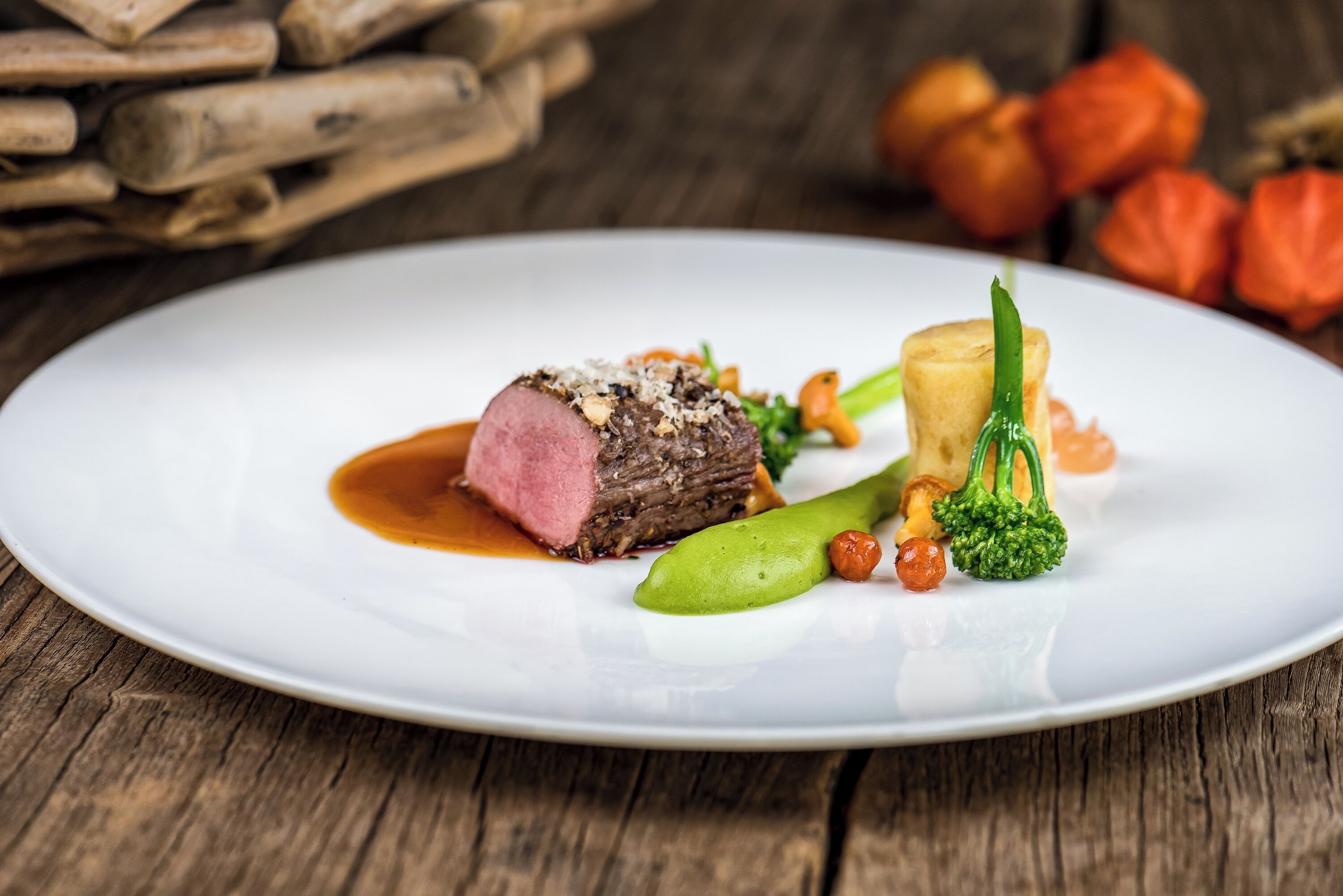 A white plate with a piece of meat, green vegetables, and a sauce.
