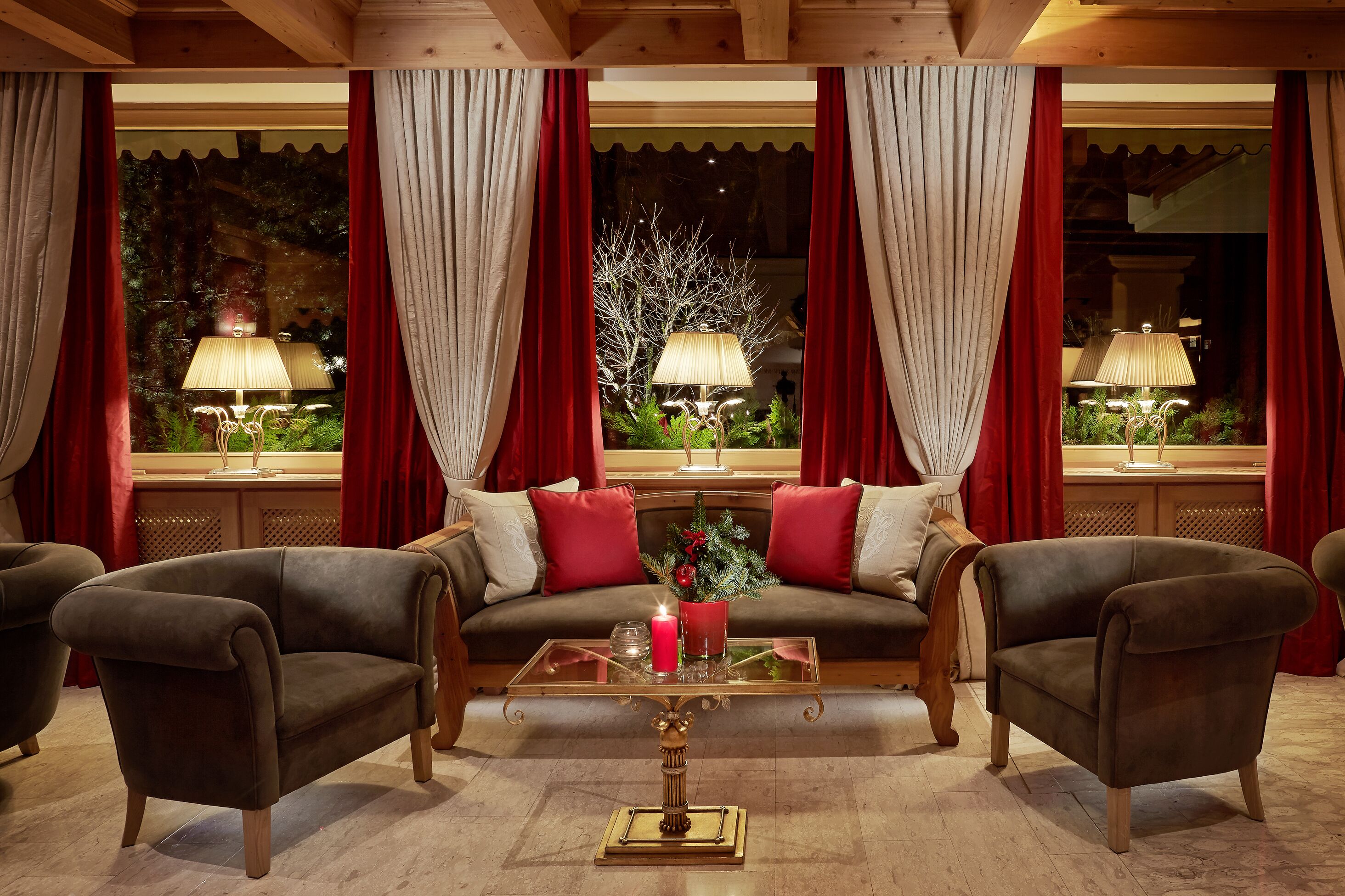 Una habitación acogedora con sofá, dos sillones, una mesita de centro de cristal y cortinas rojas.