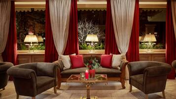 Una habitación acogedora con sofá, dos sillones, una mesita de centro de cristal y cortinas rojas.