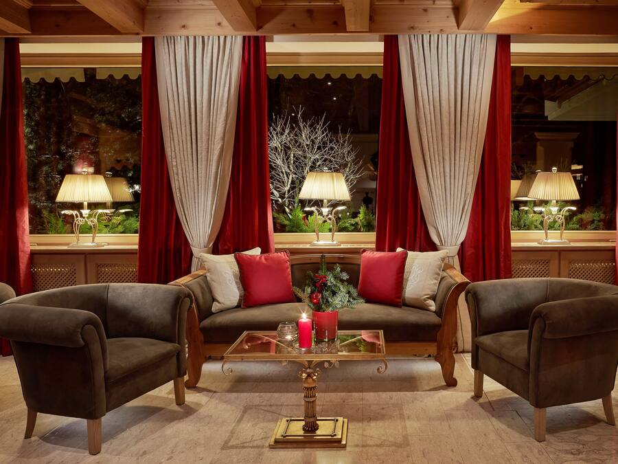 Una habitación acogedora con sofá, dos sillones, una mesita de centro de cristal y cortinas rojas.