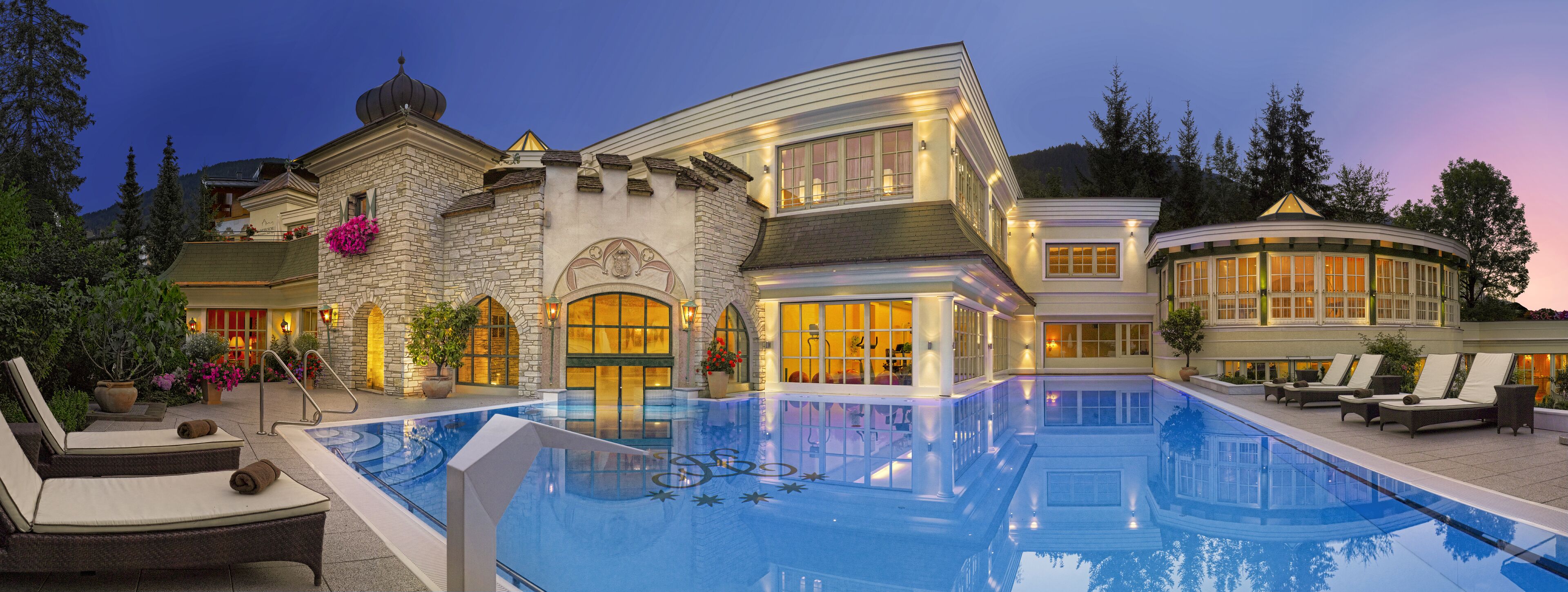 A luxurious pool area with a stone building, a gazebo, and lounge chairs.
