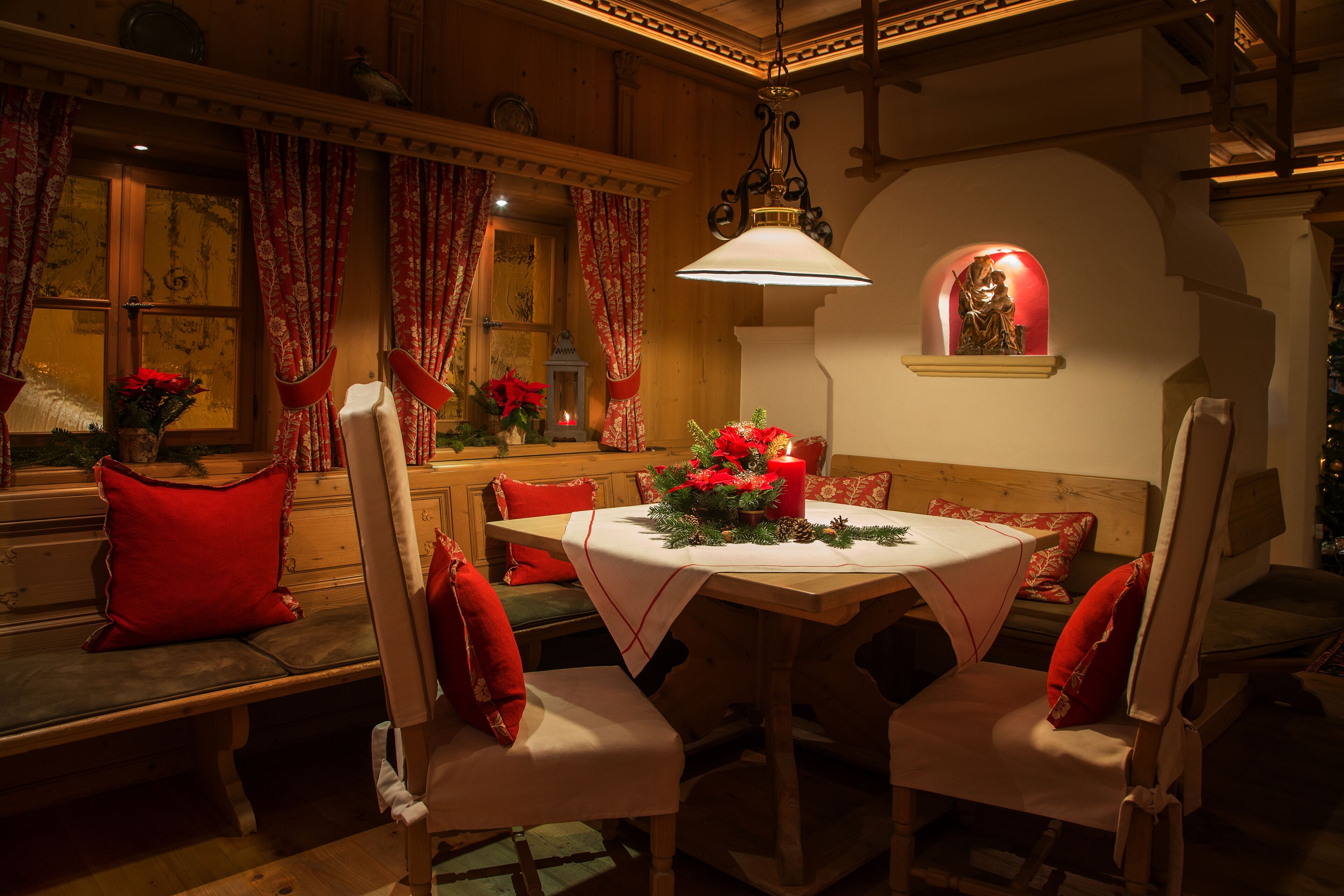 A warmly lit dining area with a round table, white chairs, and red cushions.