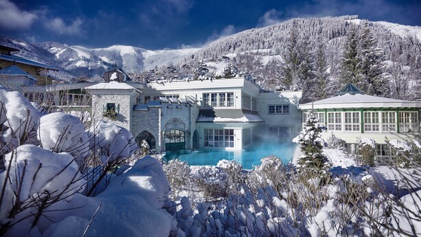 Un resort cubierto de nieve con piscina, edificios de piedra y montañas al fondo.