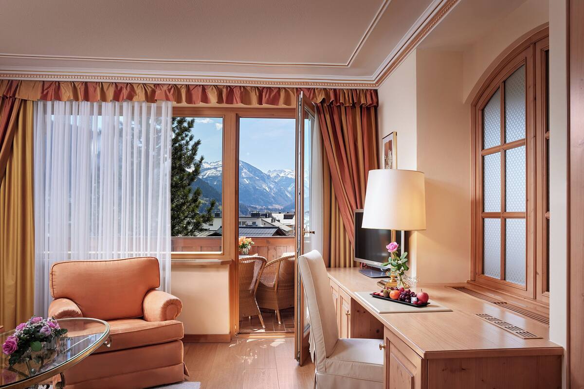 Een hotelkamer met uitzicht op bergen, een bank, een bureau met lamp en een televisie.