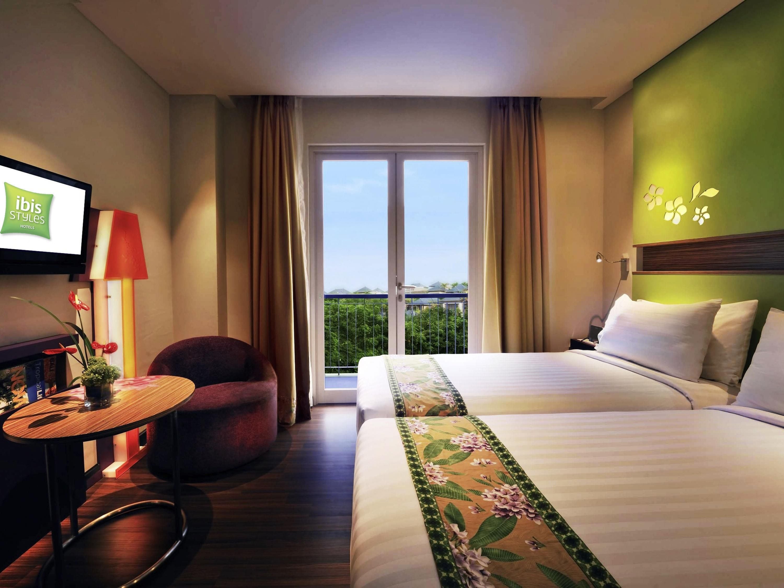 Habitación de hotel con cama, una silla, una mesita, televisión y balcón con vistas.