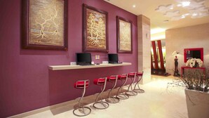 A reception area with purple walls, three framed artworks, a row of red bar stools, and a reception desk with two laptops. - ibis Styles Bali Denpasar (Denpasar)