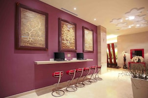 A reception area with purple walls, three framed artworks, a row of red bar stools, and a reception desk with two laptops.