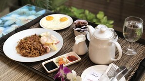 A tray with a plate of noodles, fried eggs, and a small dish of vegetables, a teapot, a glass of water, and a cup of tea. - ibis Styles Bali Denpasar (Denpasar)