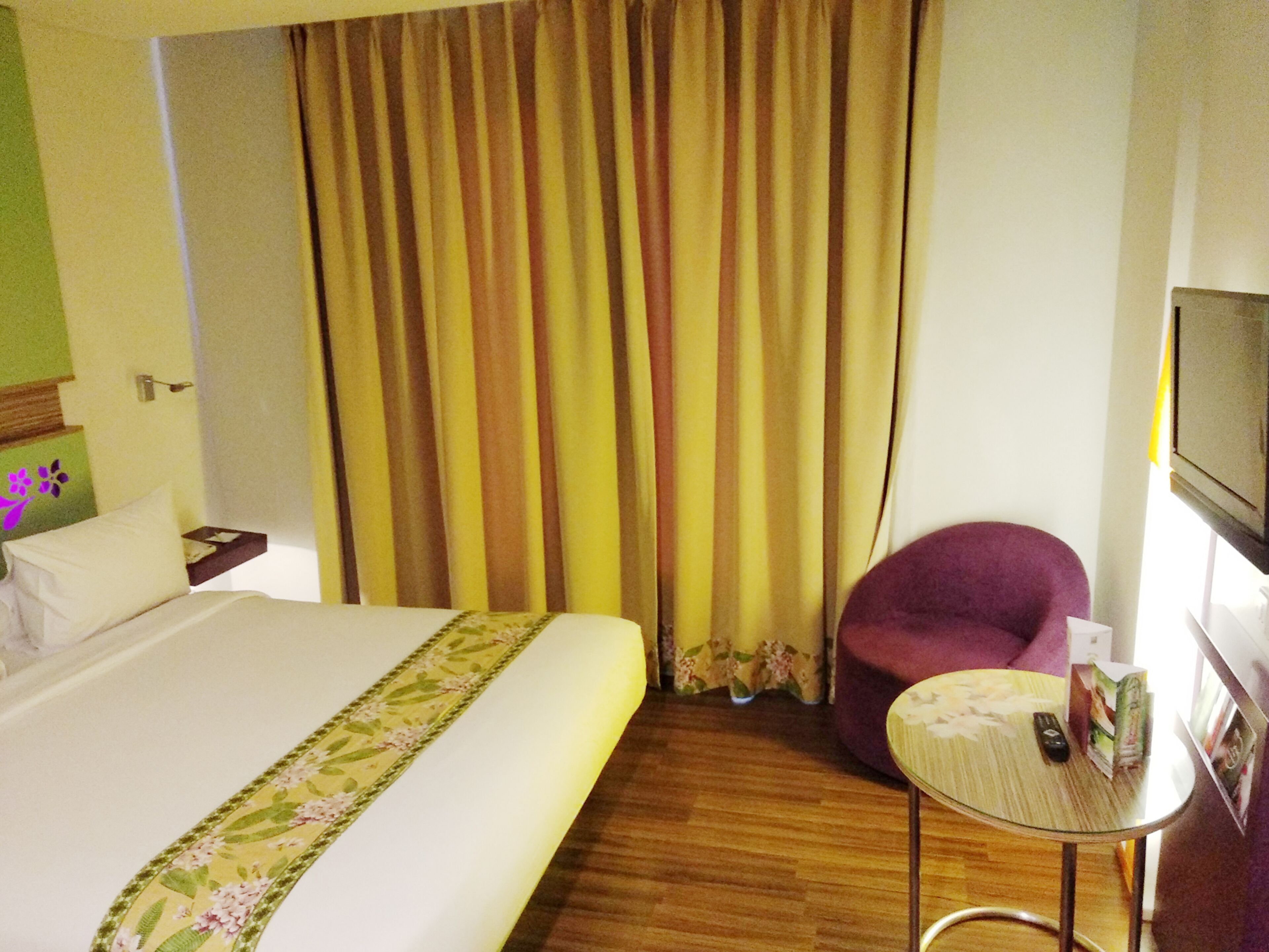 Ein Hotelzimmer mit einem Bett, einem kleinen Tisch, einem violetten Sessel und einem Fernseher an der Wand.