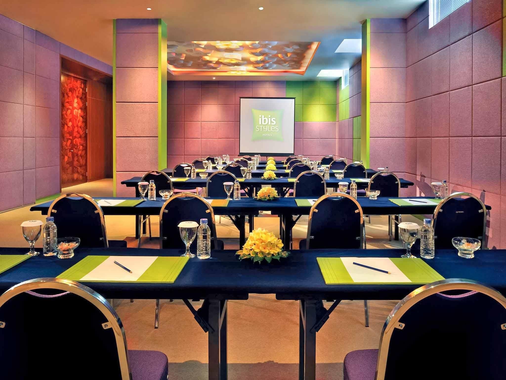 Un salón de conferencias con varias mesas, sillas y una pantalla para presentaciones.