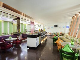 Un moderno vestíbulo de hotel con un bufé central, zonas de estar y un televisor montado en la pared.