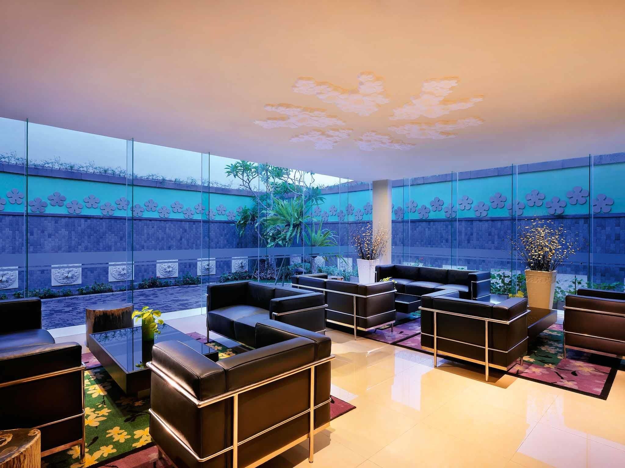 Un espacio exterior moderno con sofás de cuero y mesas, un techo decorativo y una pared con motivos florales.