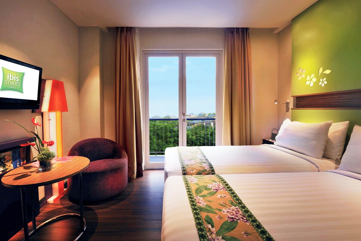 Una habitación de hotel con cama, una silla, una mesita, televisión y balcón con vistas.