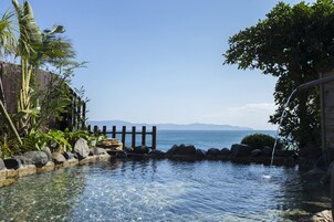 Una piscina cristalina con cerramiento de madera, rodeada de rocas y plantas tropicales, que da a vistas del mar.