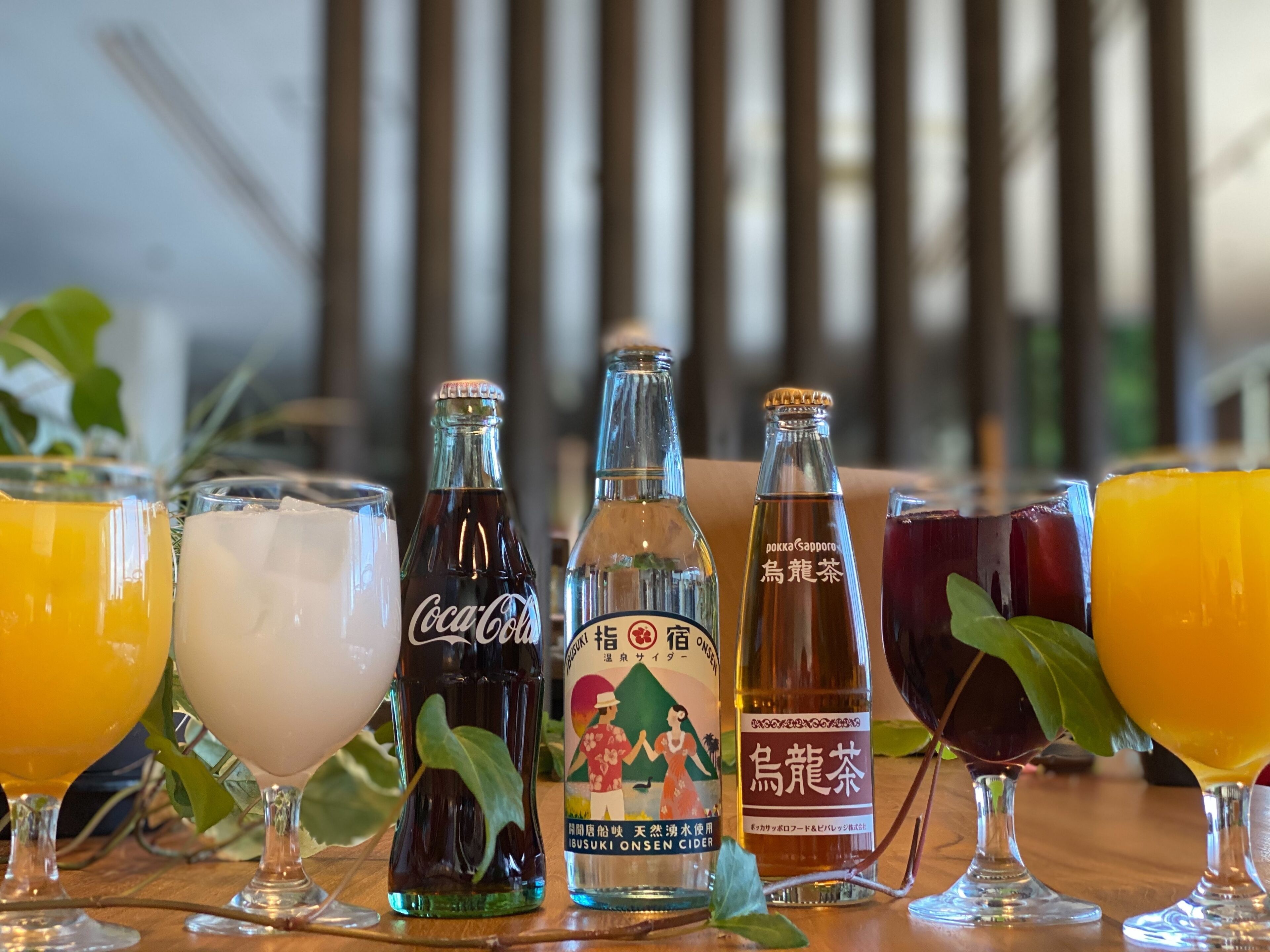 Une sélection de boissons comprenant du Coca-Cola, une bouteille de saké japonais et une bouteille de vin de prune japonais, le tout servi dans des verres transparents.