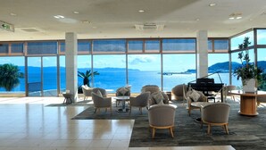 A spacious lobby with large windows offering a view of the sea and mountains. There are several seating areas with chairs and tables. - Ibusuki Royal Hotel (Ibusuki)