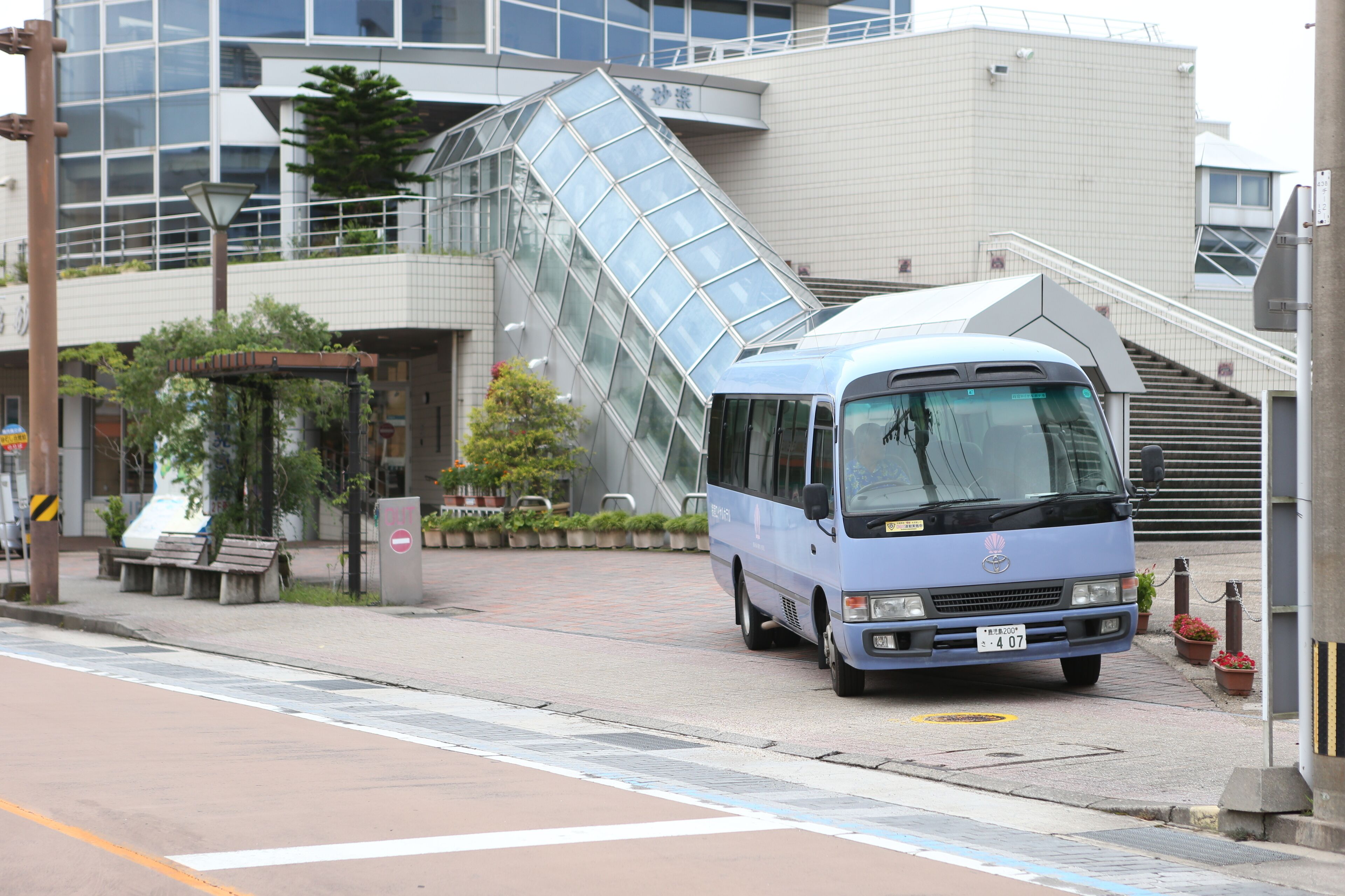A blue bus parked in front of a modern building with a glass facade and a staircase leading to an upper level.