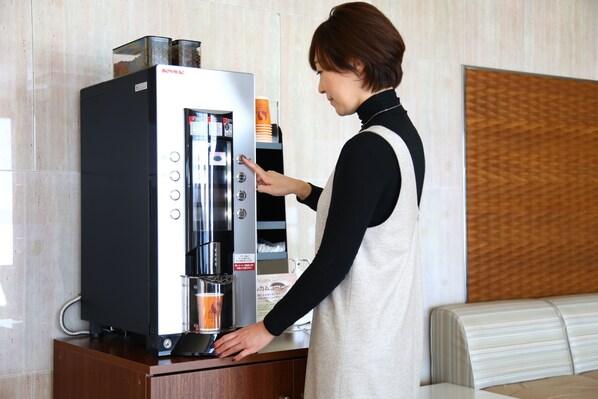 Una persona usando una máquina de café en una habitación con pared de paneles de madera y un banco acolchado.