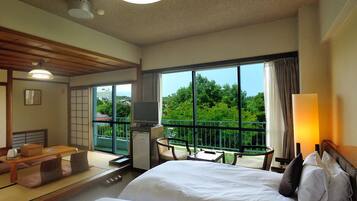 Habitación de hotel con dos camas, una mesa de comedor, televisión y balcón con vista a zonas verdes.