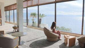 A spacious lobby with large windows offering a view of the sea and mountains. There are comfortable seating areas and a small table. - Ibusuki Royal Hotel (Ibusuki)