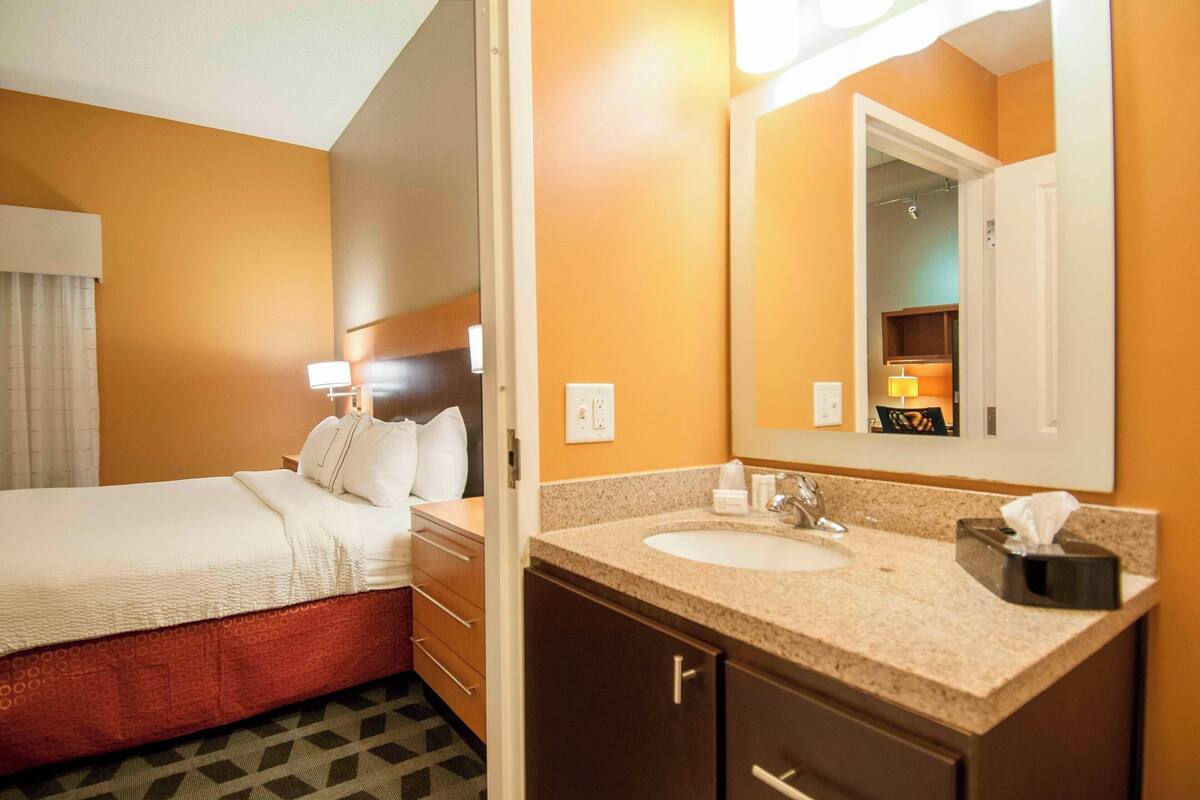 A hotel room with a bed, a bathroom with a sink, and a mirror.