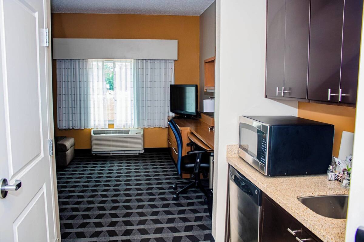 A compact hotel room with a kitchenette, a small desk with a computer, a television, and a microwave.