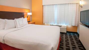 A hotel room with a large bed, a bedside table with a lamp, a window with curtains, and a television on the wall.