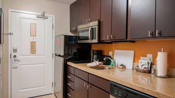 A compact kitchen with dark brown cabinets, a stainless steel microwave, a coffee maker, and a dishwasher.