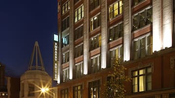 A multi-story hotel with a classic architectural design, featuring a prominent corner tower and a well-lit facade.