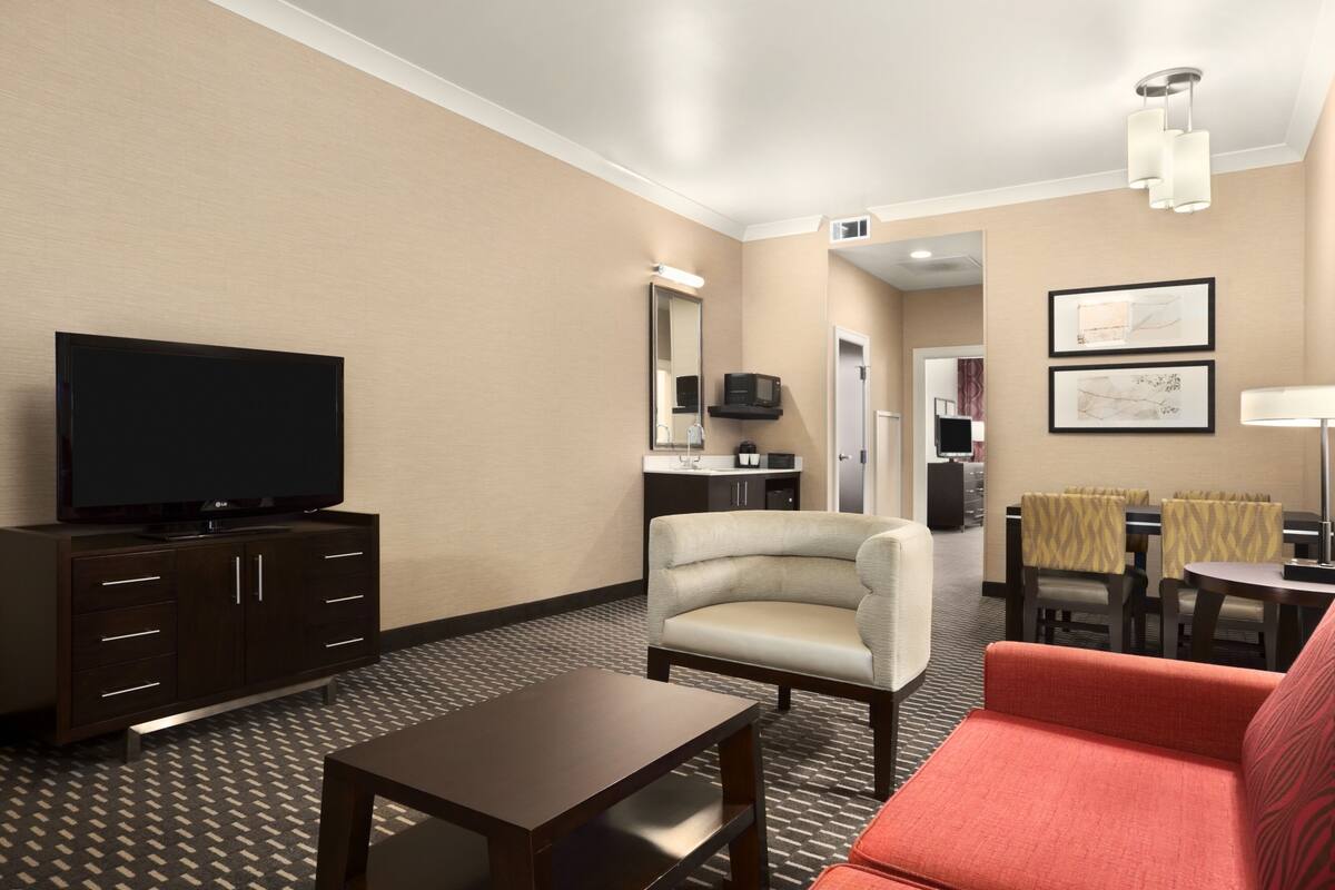Una habitación de hotel con televisión, sofá, mesa de comedor y una silla.