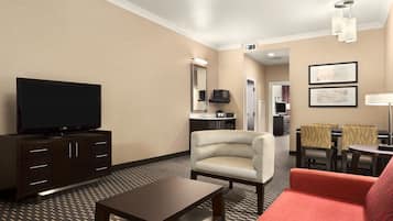 A hotel room with a TV, a sofa, a dining table, and a chair.