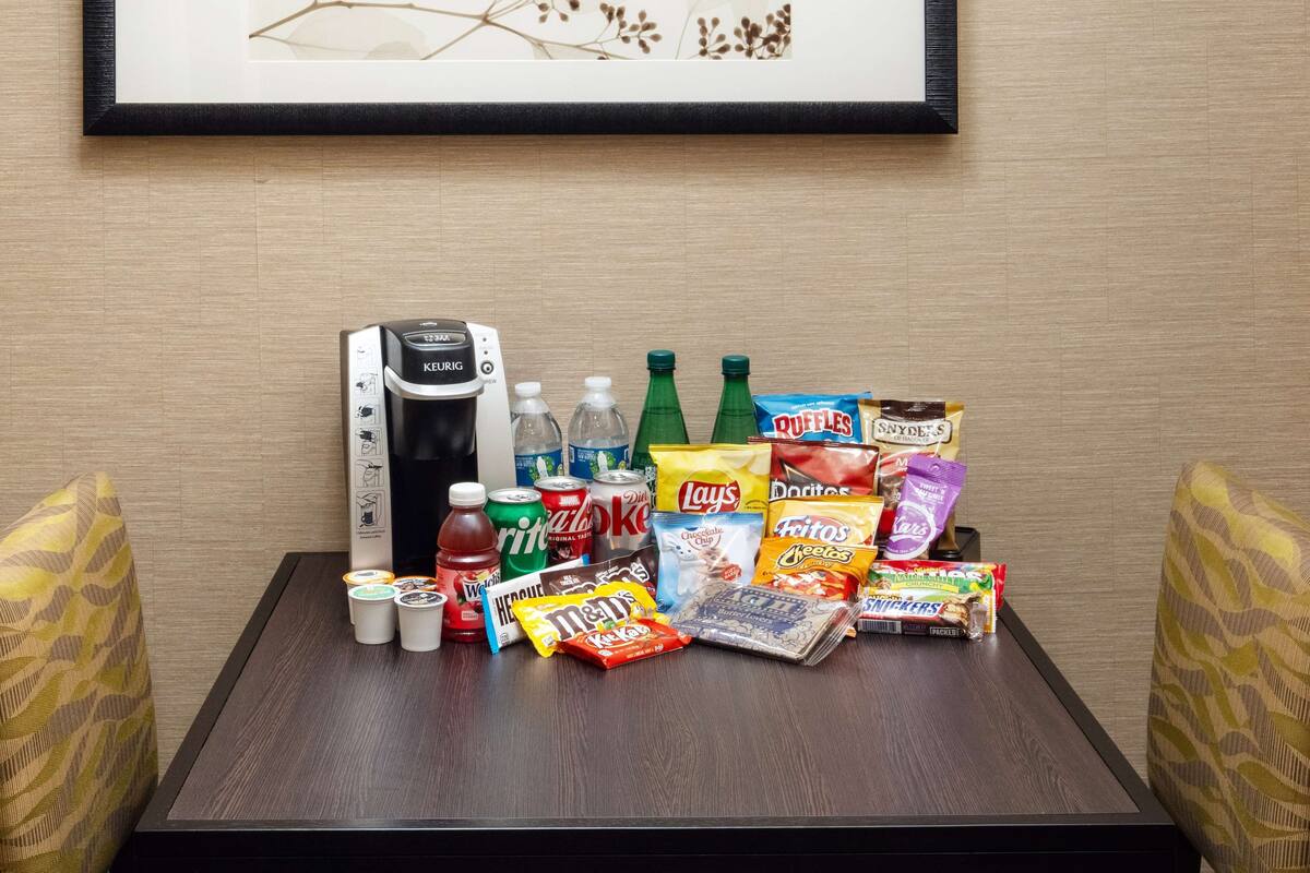 Una mesa con bocadillos, bebidas y una cafetera Keurig.