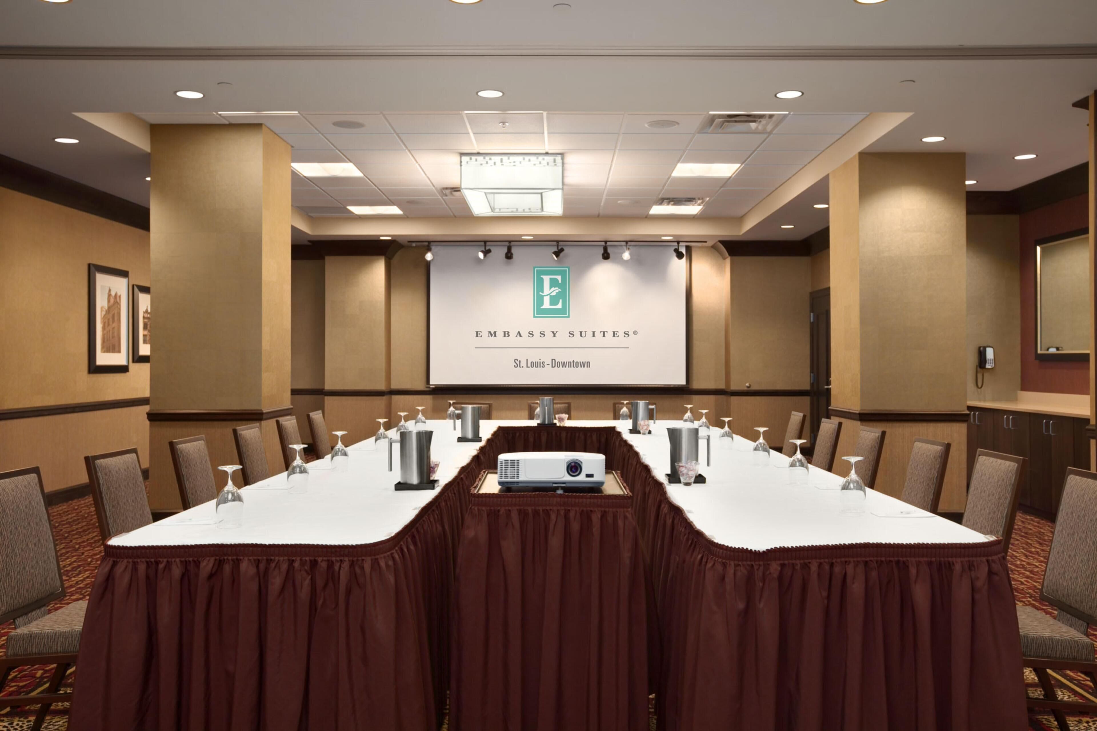 Una sala conferenze con un lungo tavolo, sedie, un proiettore e uno schermo per presentazioni.