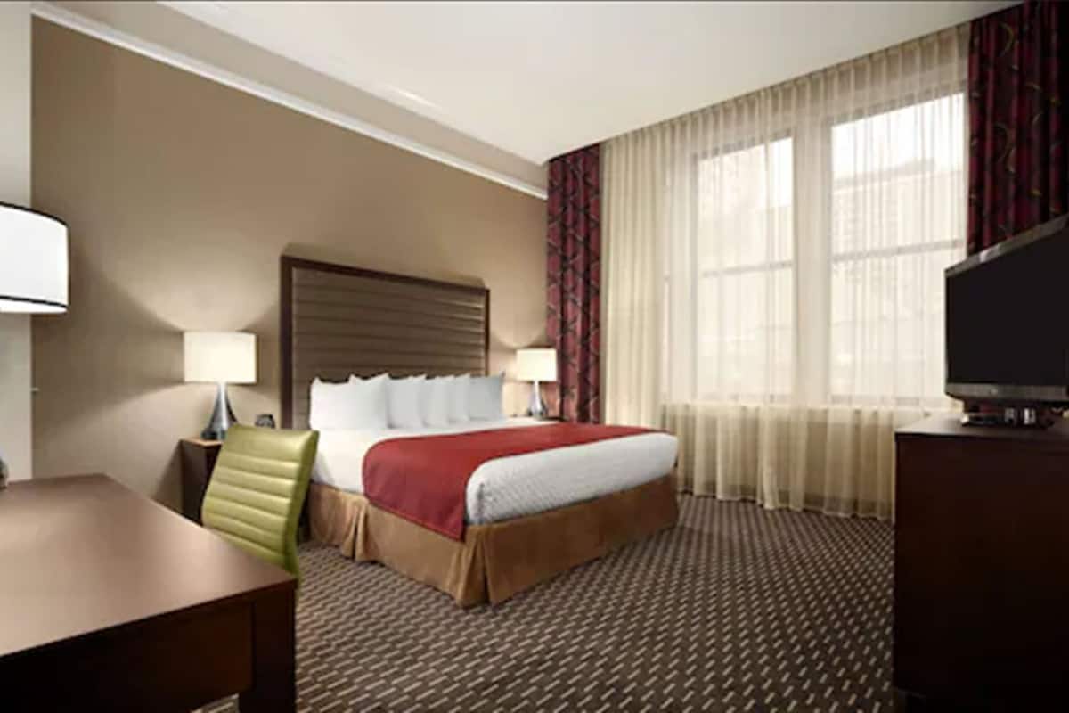 Una habitación de hotel con una cama, un escritorio, una silla, un televisor y una ventana con cortinas.