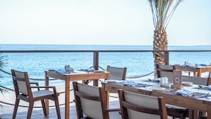 Une terrasse en bois, avec des tables et des chaises, donnant sur la mer.