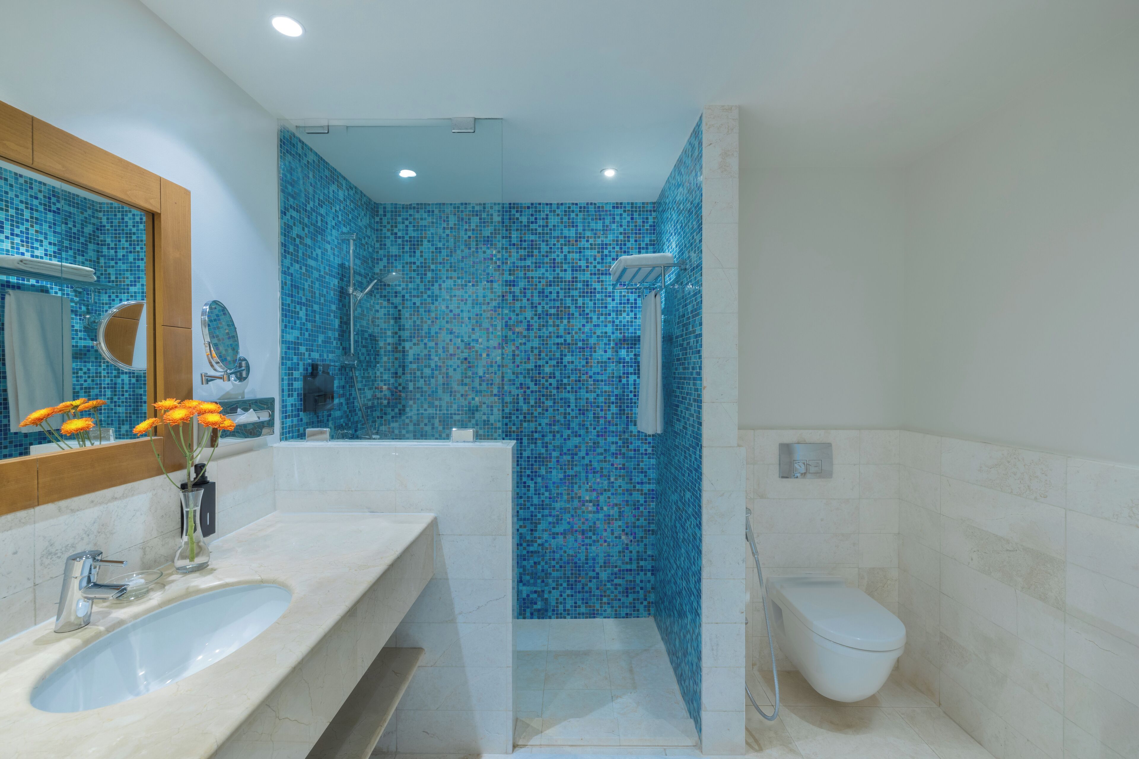 Un baño con un lavamanos grande, espejo y zona de ducha con mosaicos azules.