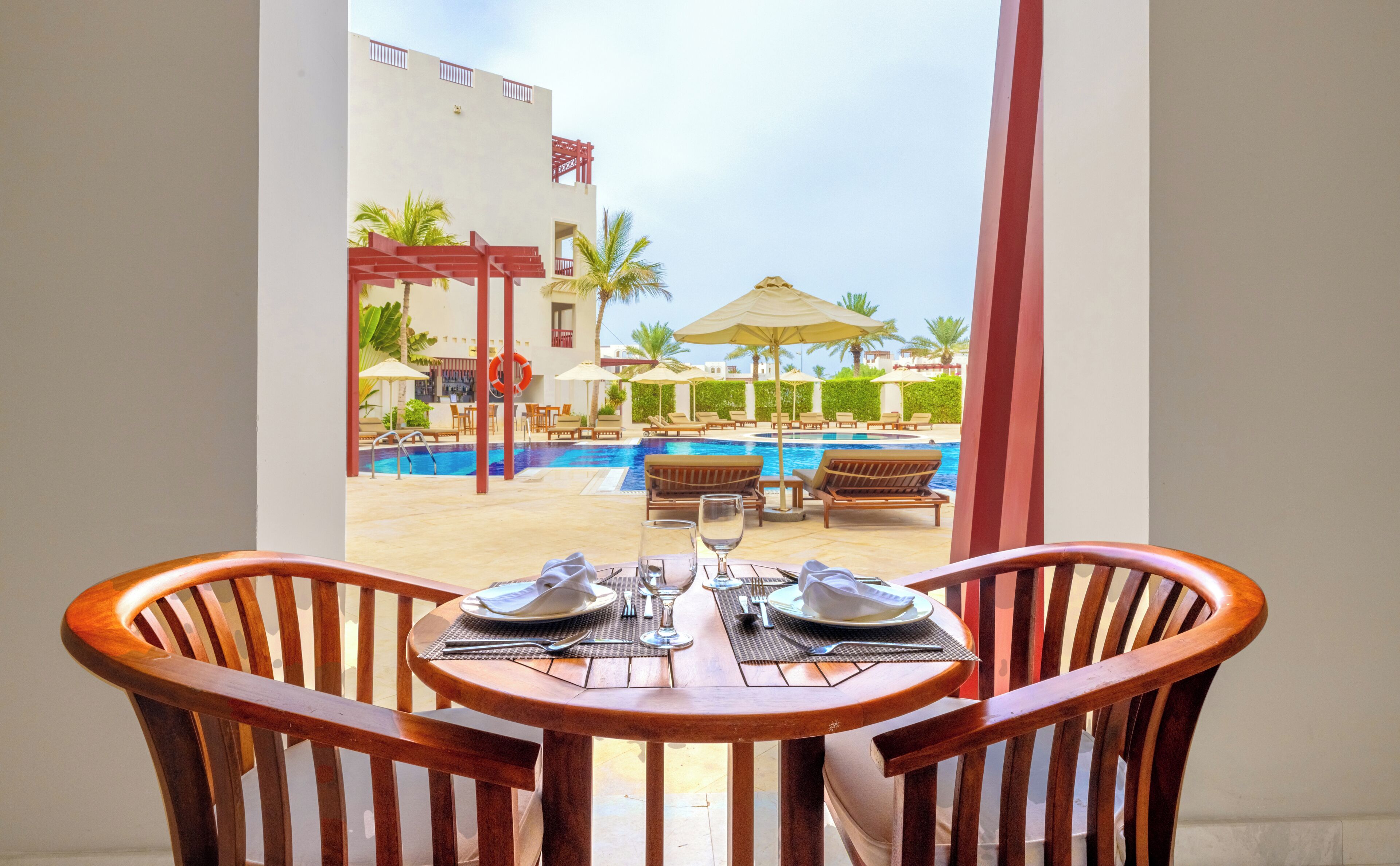 Une table à manger avec des chaises, une piscine et des chaises longues à l’arrière-plan.