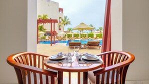 A dining table with chairs, a pool, and lounge chairs in the background. - Sifawy Boutique Hotel (As Sifah)