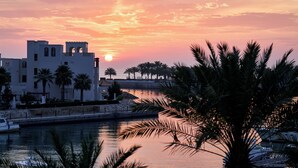 Une propriété située au bord de l’eau, avec un bâtiment blanc, des palmiers et un coucher de soleil.