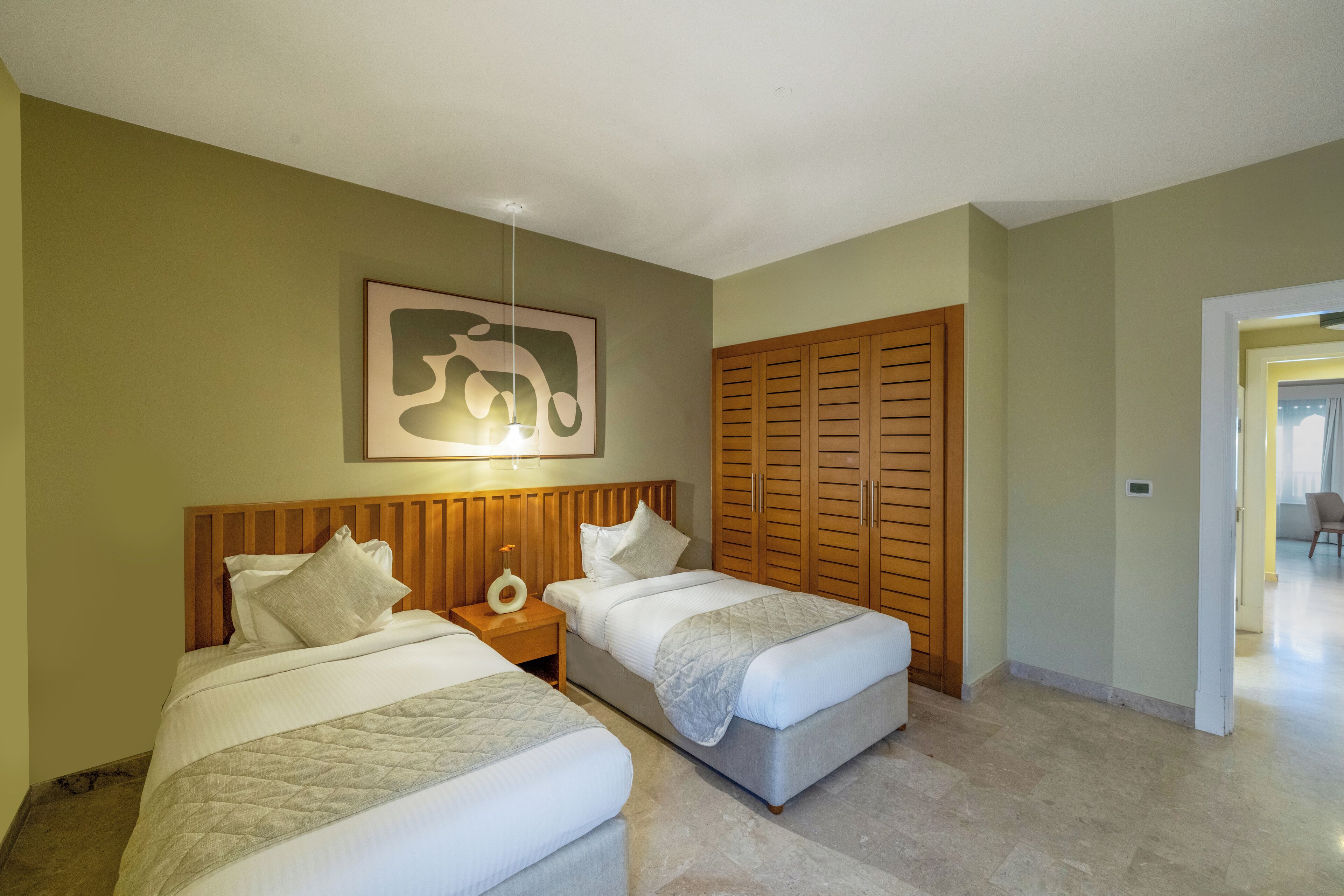 A hotel room with two beds, a wooden headboard, a bedside table with a lamp, and a large framed picture on the wall.