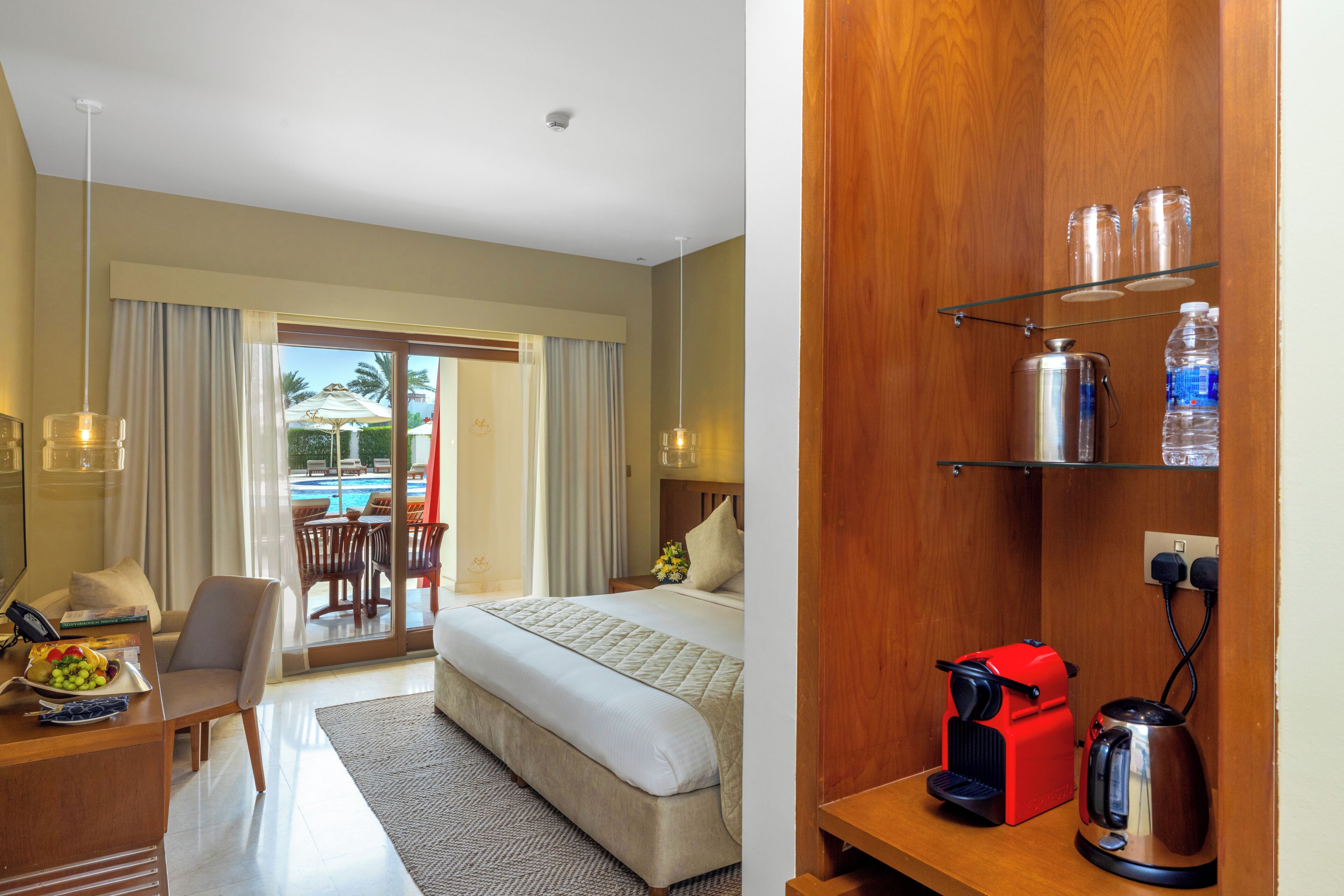 Une chambre d’hôtel avec un lit, un bureau doté d’un téléphone, une machine à café et une bouteille d’eau posée sur une étagère.