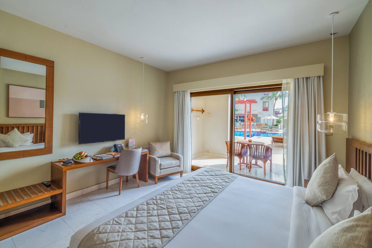 Une chambre d’hôtel équipée d’un lit, d’un bureau, d’une chaise, d’une télévision et offrant une vue sur l’espace extérieur de la piscine.