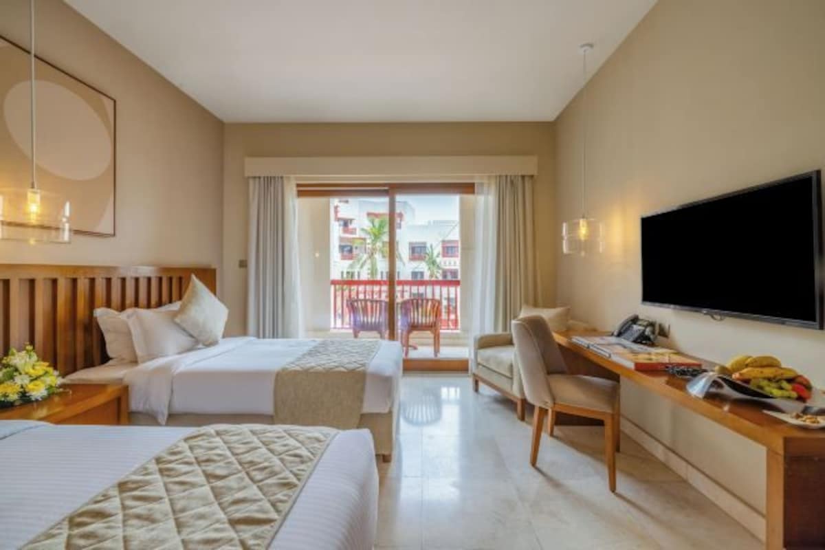 Une chambre d’hôtel avec deux lits, un bureau, une télévision et un balcon donnant sur des immeubles.
