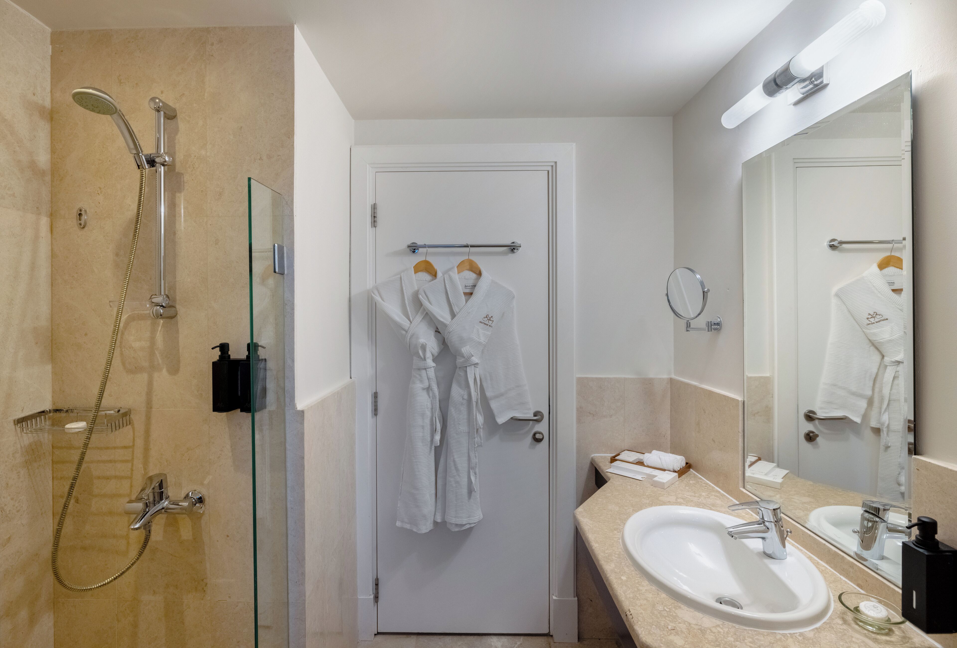 A bathroom with a glass-enclosed shower, a white door with a towel rack, and a sink with a mirror.