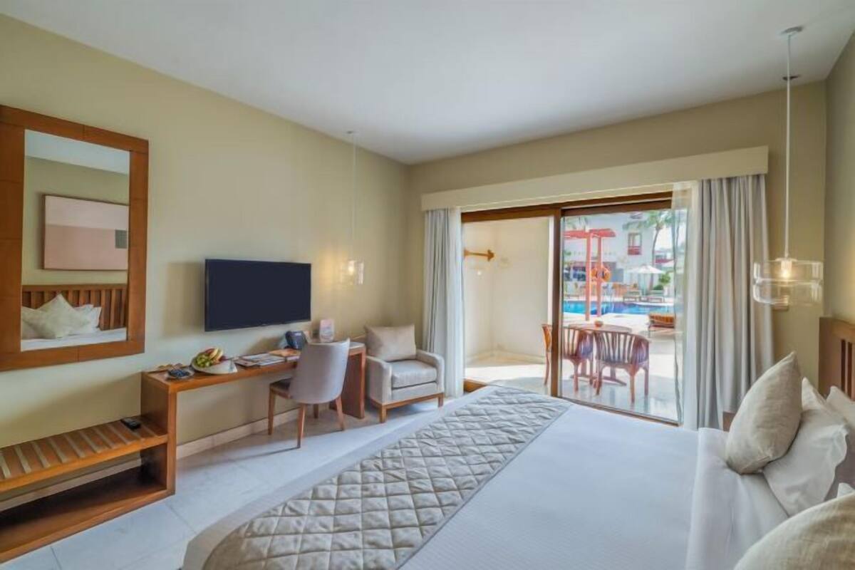 Une chambre d’hôtel avec un grand lit, un bureau avec une chaise, une télévision et une vue sur l’espace extérieur de la piscine.
