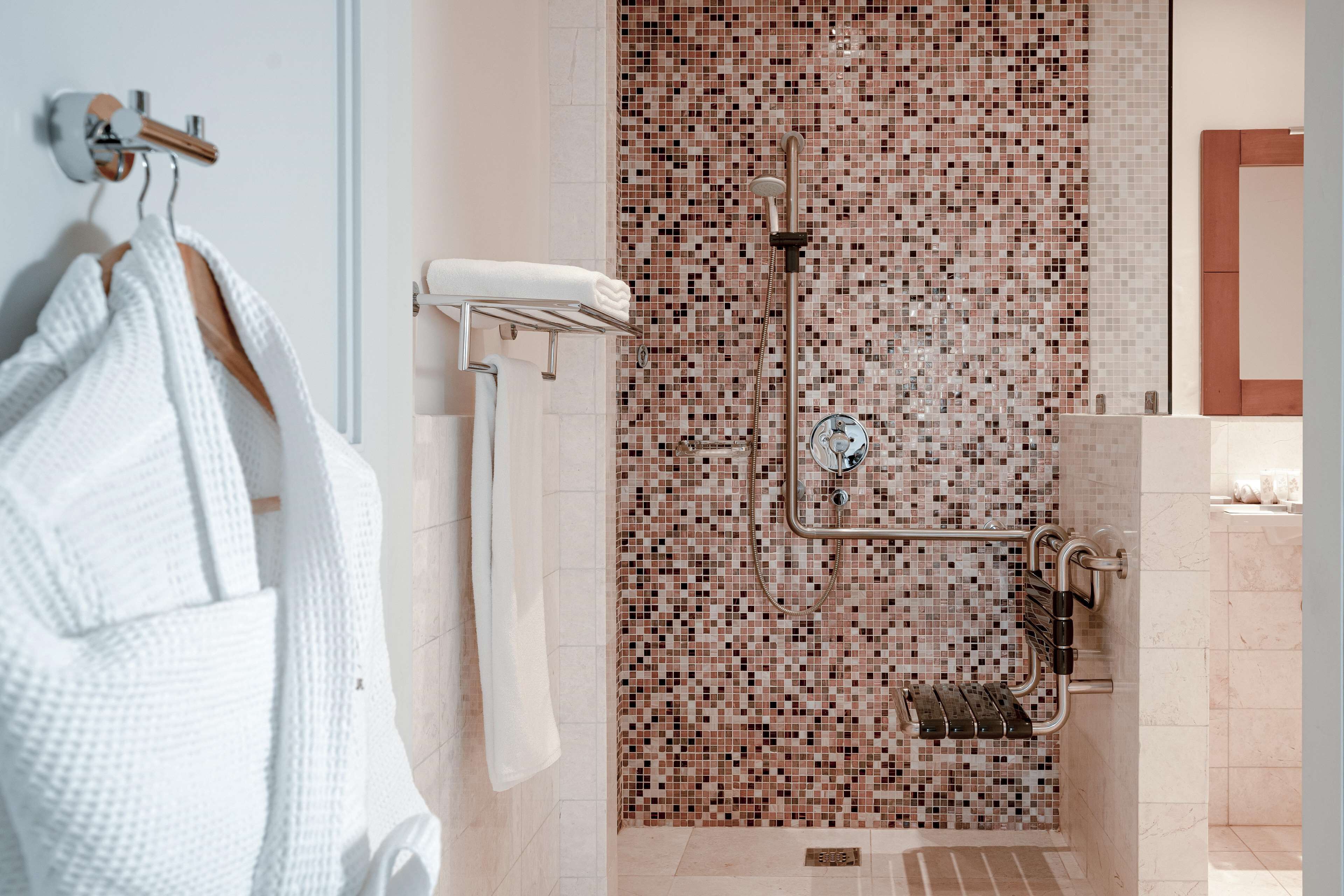 A modern bathroom with a mosaic tile shower wall, a towel rack with white towels, and a visible toilet paper holder.