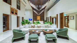 Un hall d’entrée spacieux avec un plafond haut, un espace de détente central comprenant un canapé et des fauteuils, ainsi qu’un lustre décoratif.