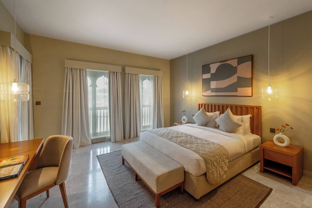 Une chambre d’hôtel moderne, dotée d’un grand lit, d’un bureau et offrant une vue sur l’extérieur grâce à ses fenêtres.