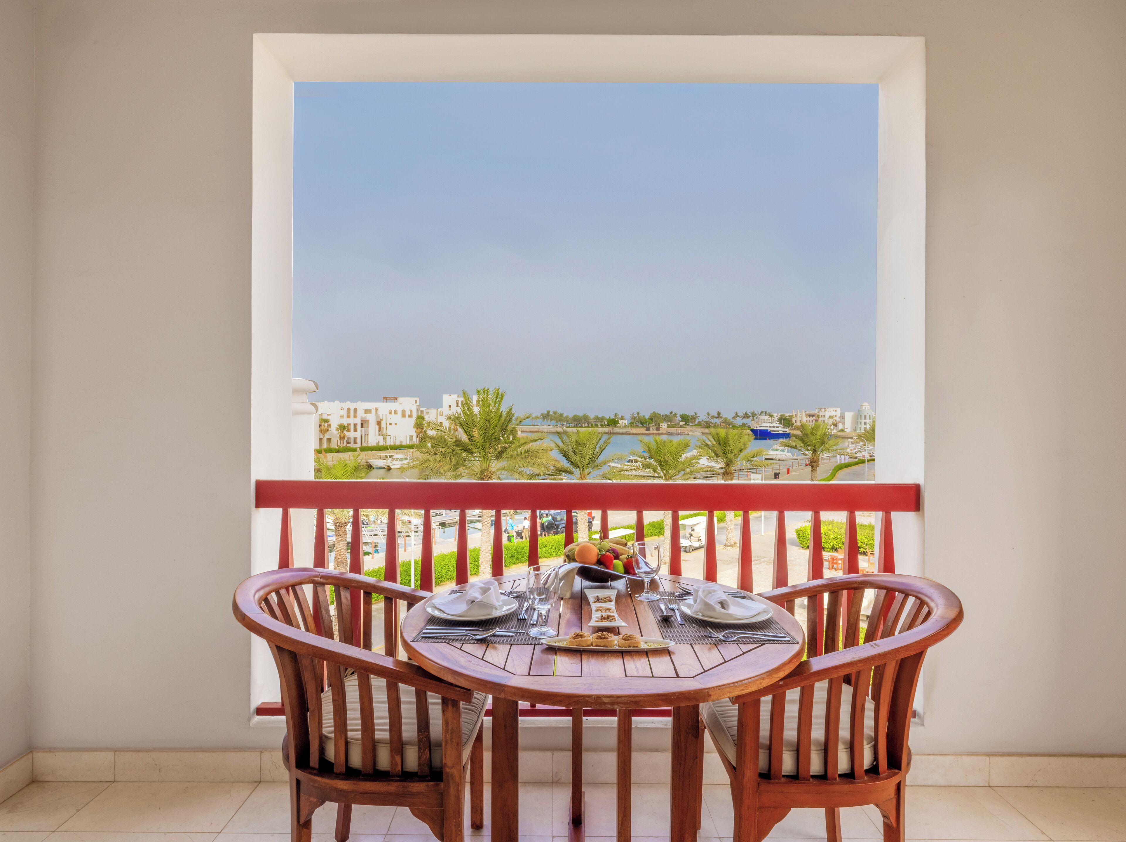 Un balcon avec une table dressée pour deux personnes, donnant sur une marina et des immeubles.